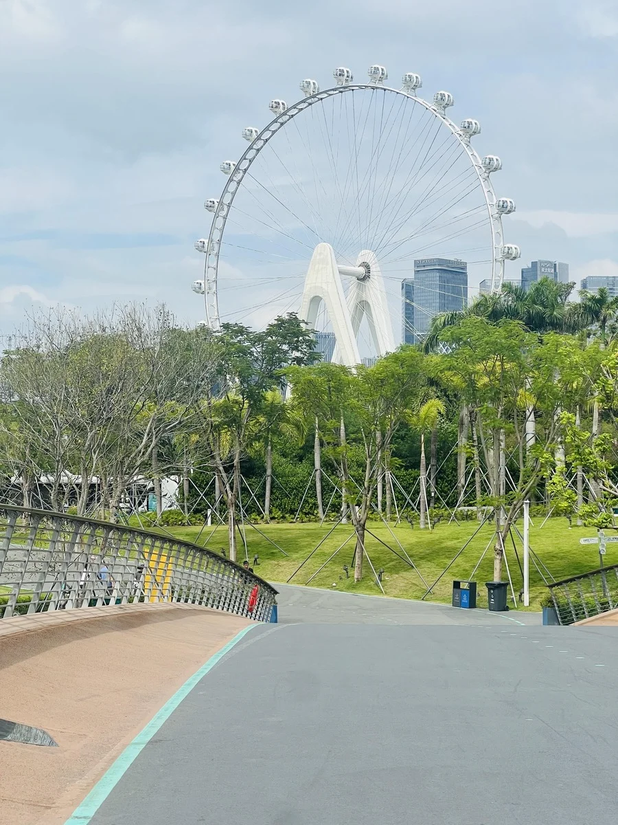 A scenic view of the giant white Ferris wheel at Happy Harbor, with lush green parkland and modern skyscrapers in the backgro