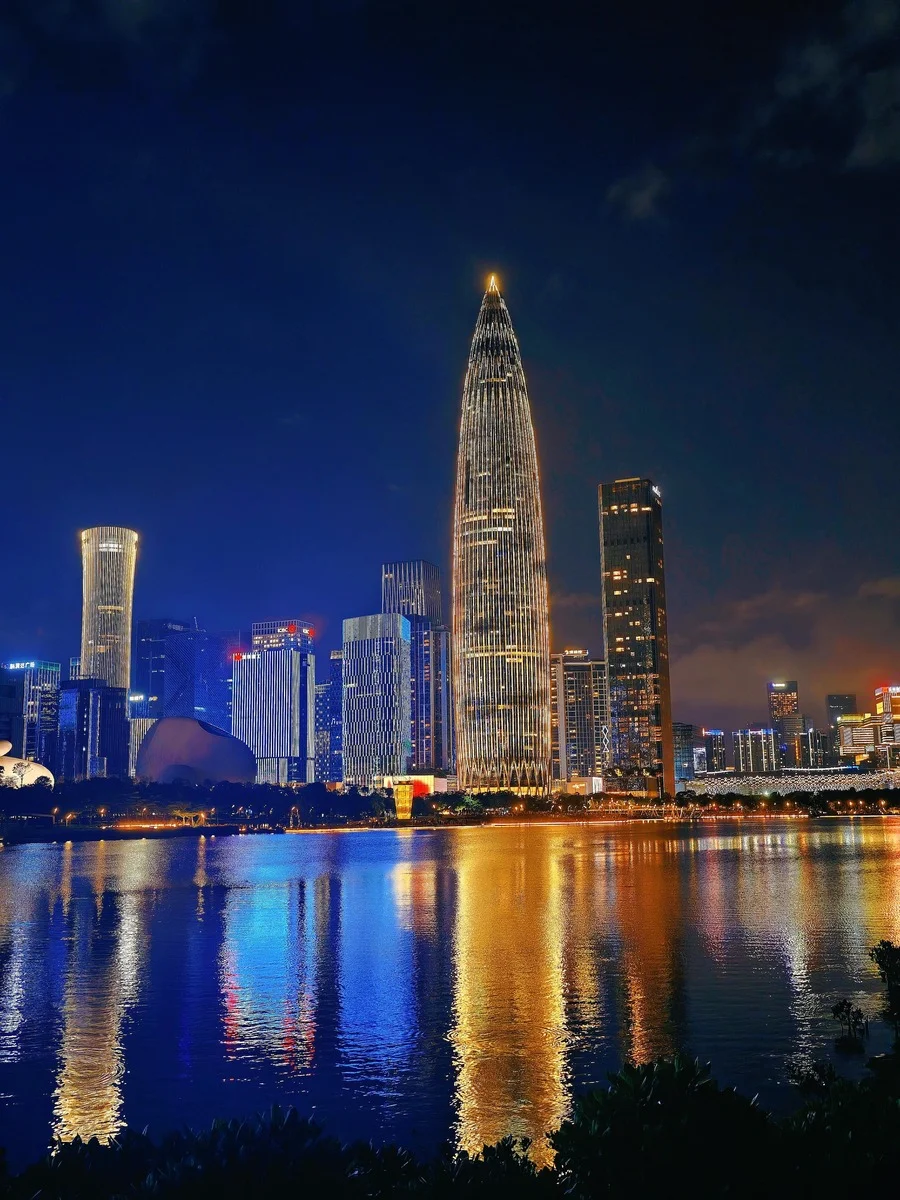 Nighttime city skyline of Shenzhen with illuminated skyscrapers reflecting on the water at Talent Park.