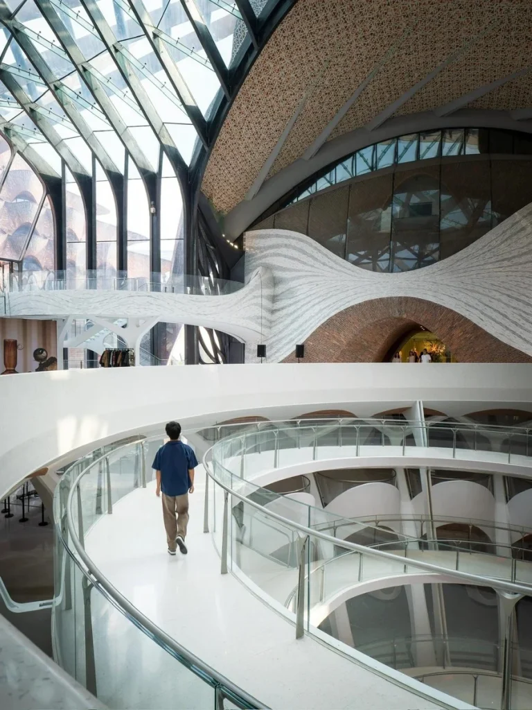 A person walking along a futuristic, white curved walkway inside a modern architectural space with flowing concrete forms, gl