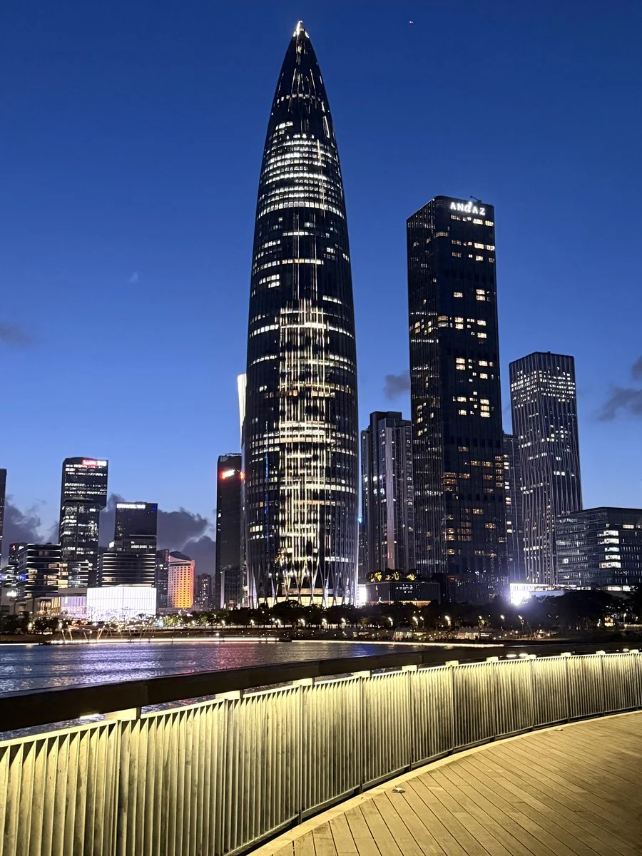 Nighttime cityscape of Shenzhen featuring the iconic CITIC Tower and surrounding skyscrapers, reflected in the water with a l