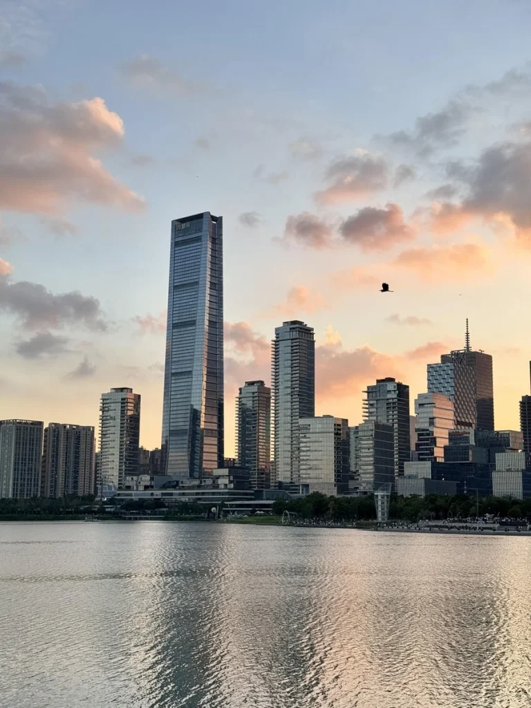 Sunset city skyline with Qinchuan Tower reflected in the lake at Rencai Park, Shenzhen.